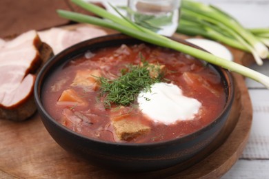 Photo of Tasty borscht with sour cream in bowl served with green onion on white wooden table, closeup