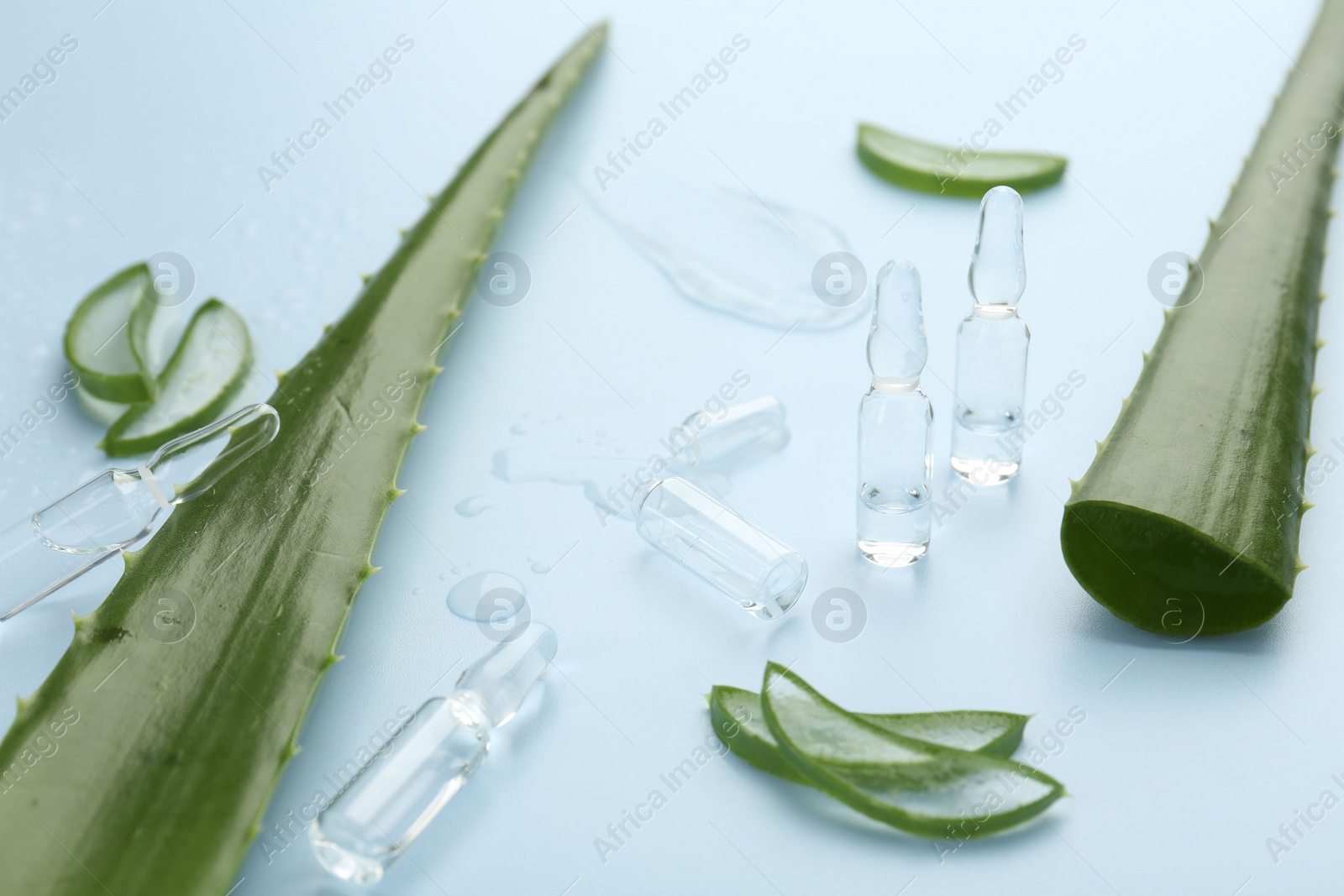 Photo of Skincare ampoules with extract of aloe vera and green leaves on light blue background, closeup