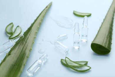 Skincare ampoules with extract of aloe vera and green leaves on light blue background, closeup