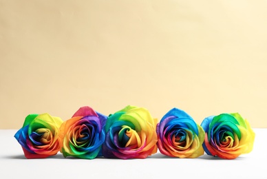 Photo of Rainbow rose flowers on table against color background