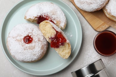 Delicious donuts with jelly and powdered sugar served on light grey table, flat lay