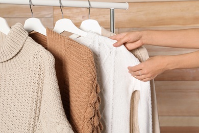 Woman choosing sweater on rack against wooden background