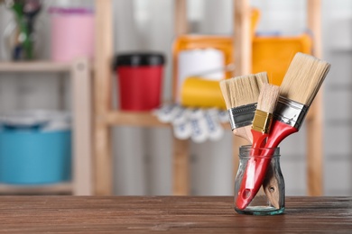 Photo of Glass jar with paint brushes on wooden table in workshop. Space for text