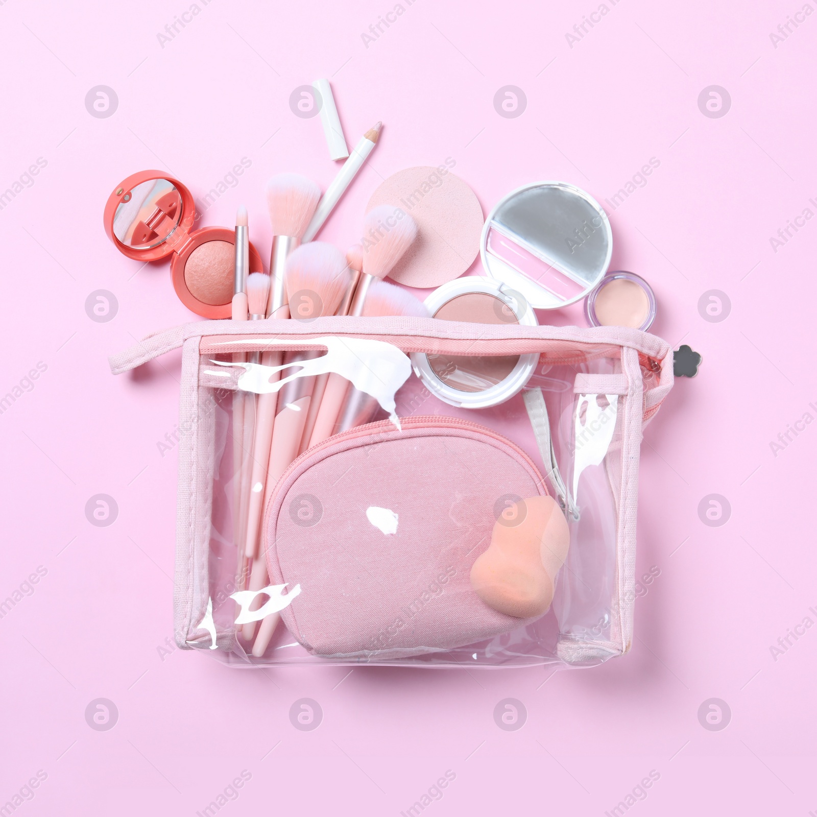 Photo of Plastic cosmetic bag with makeup products and beauty accessories on pink background, flat lay