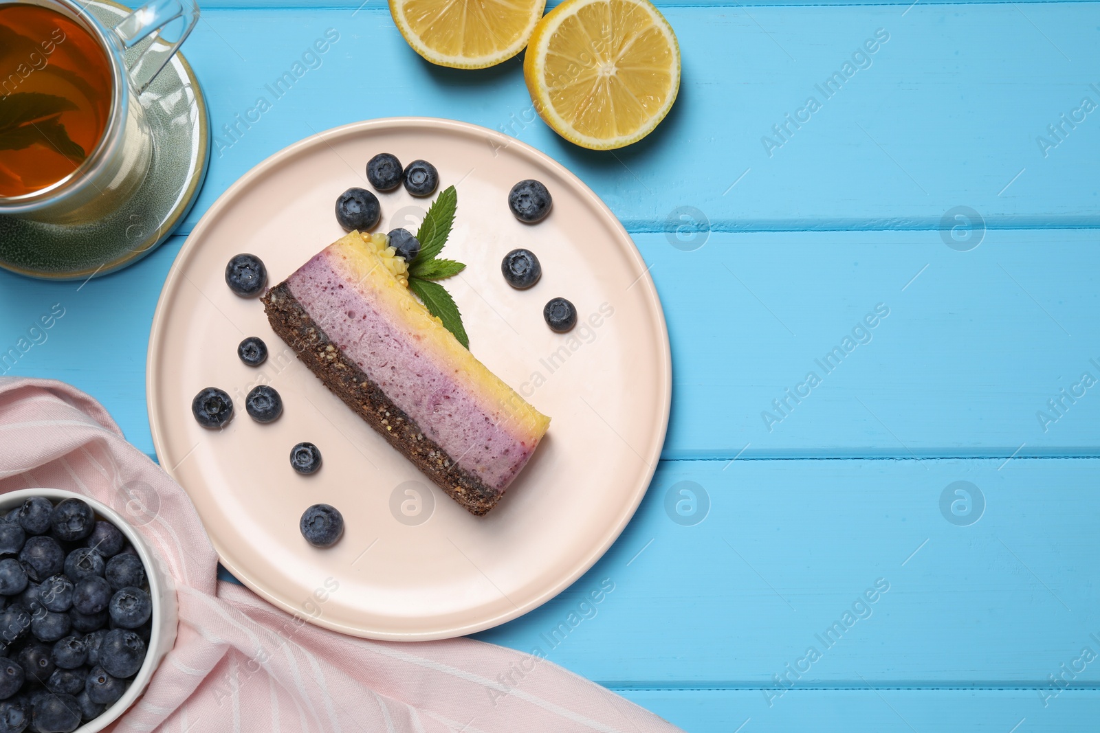 Photo of Delicious cheesecake with blueberry, lemon and tea on light blue wooden table, flat lay. Space for text