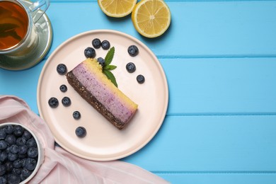 Photo of Delicious cheesecake with blueberry, lemon and tea on light blue wooden table, flat lay. Space for text