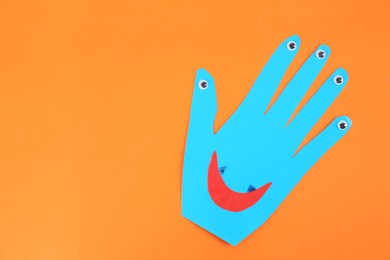 Photo of Funny blue hand shaped monster on orange background, top view with space for text. Halloween decoration