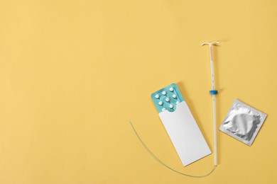 Photo of Contraception choice. Pills, condom and intrauterine device on yellow background, flat lay. Space for text