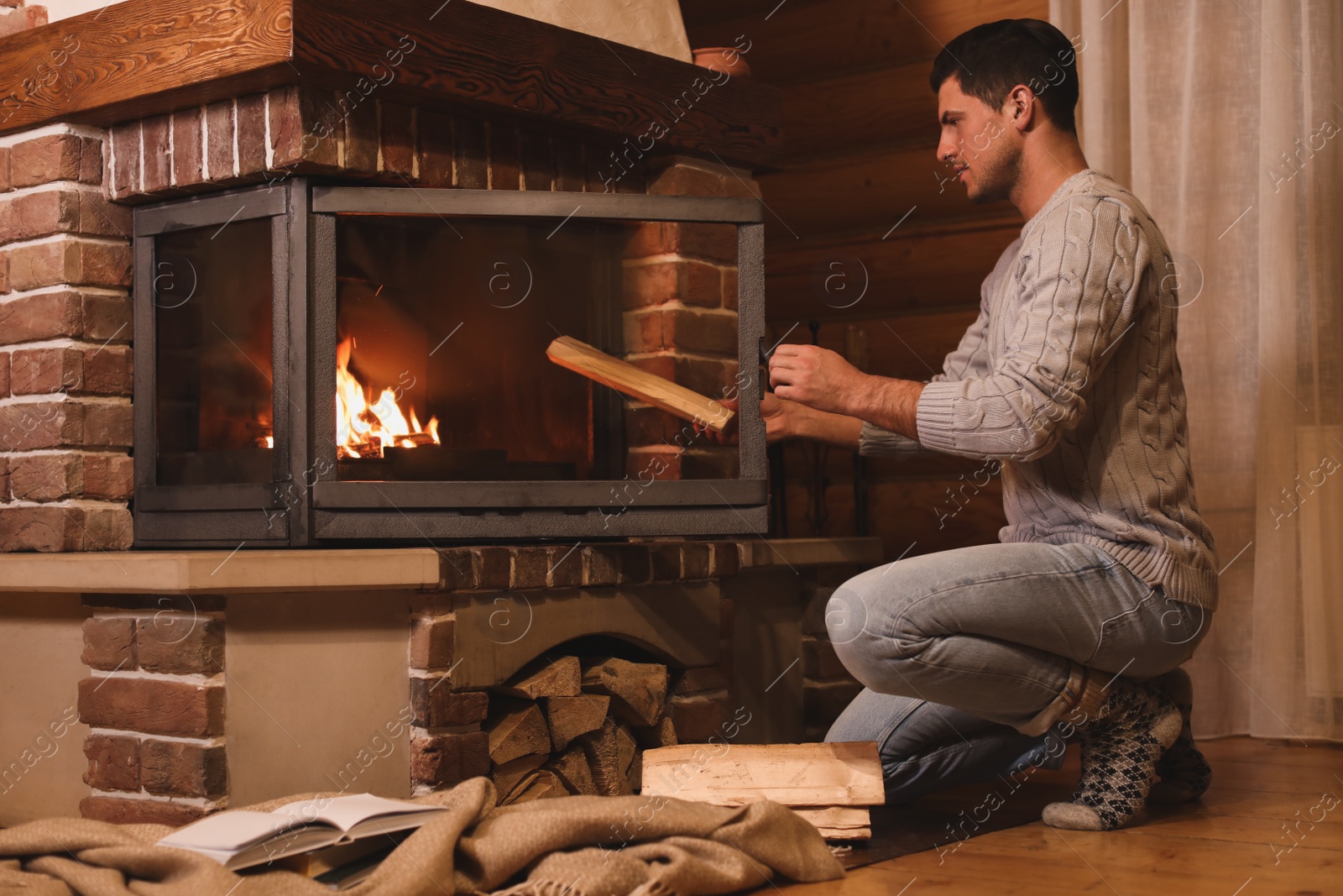 Photo of Man putting dry firewood into fireplace at home. Winter vacation