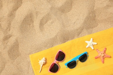 Photo of Beach accessories. Stylish sunglasses, yellow towel, starfishes and seashell on sand, top view. Space for text