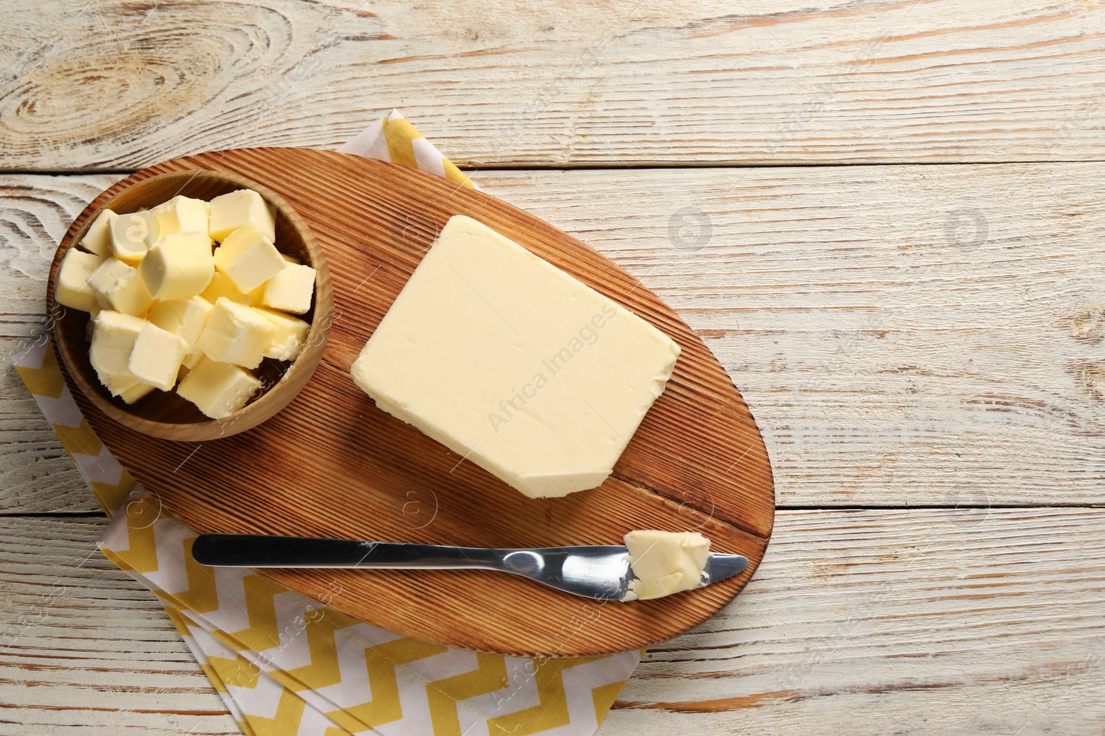 Photo of Tasty butter and knife on light wooden table, top view. Space for text