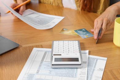 Photo of Woman with credit cards calculating taxes at wooden table, closeup
