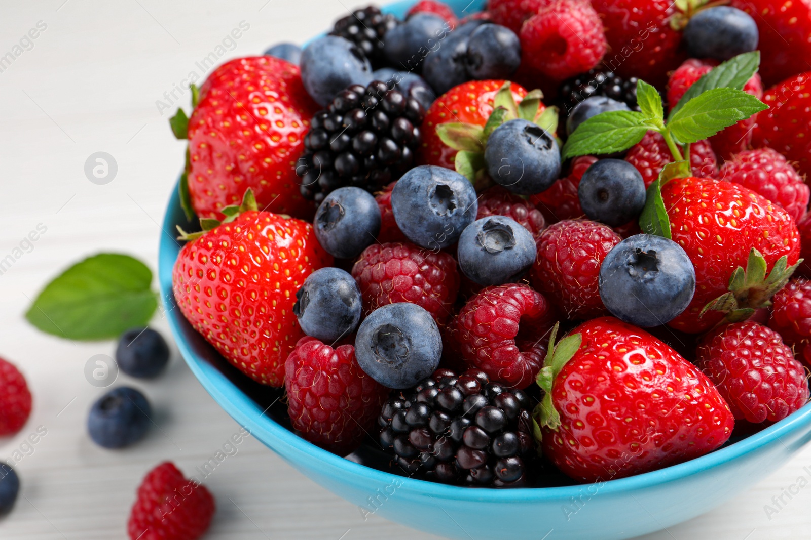 Photo of Many different fresh ripe berries in bowl on white wooden table, closeup