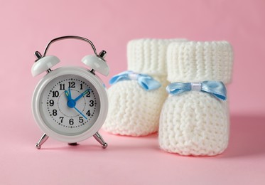 Photo of Alarm clock and baby booties on pink background. Time to give birth