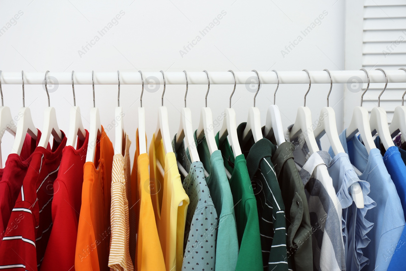 Photo of Rack with bright clothes in room. Rainbow colors