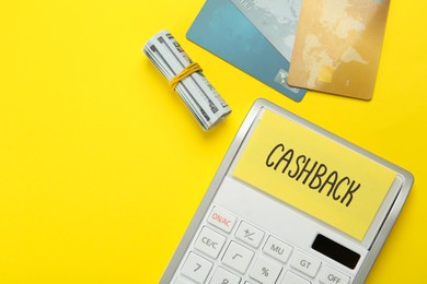 Photo of Calculator, credit card and rolled dollar banknotes on yellow background, flat lay with space for text. Cashback concept