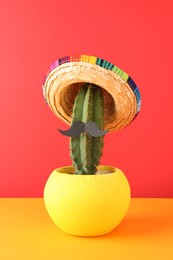 Photo of Cactus with Mexican sombrero hat and fake mustache on color background