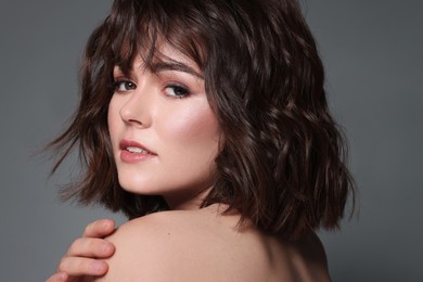 Portrait of beautiful young woman with wavy hairstyle on grey background