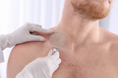 Dermatologist examining patient with magnifying glass in clinic, closeup view