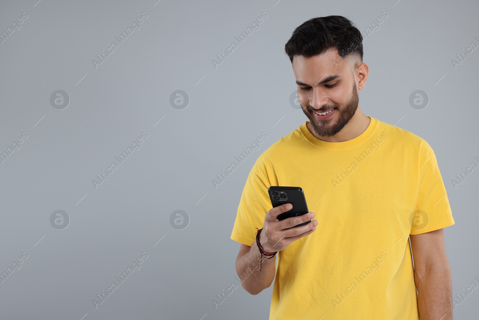 Photo of Happy young man using smartphone on grey background, space for text