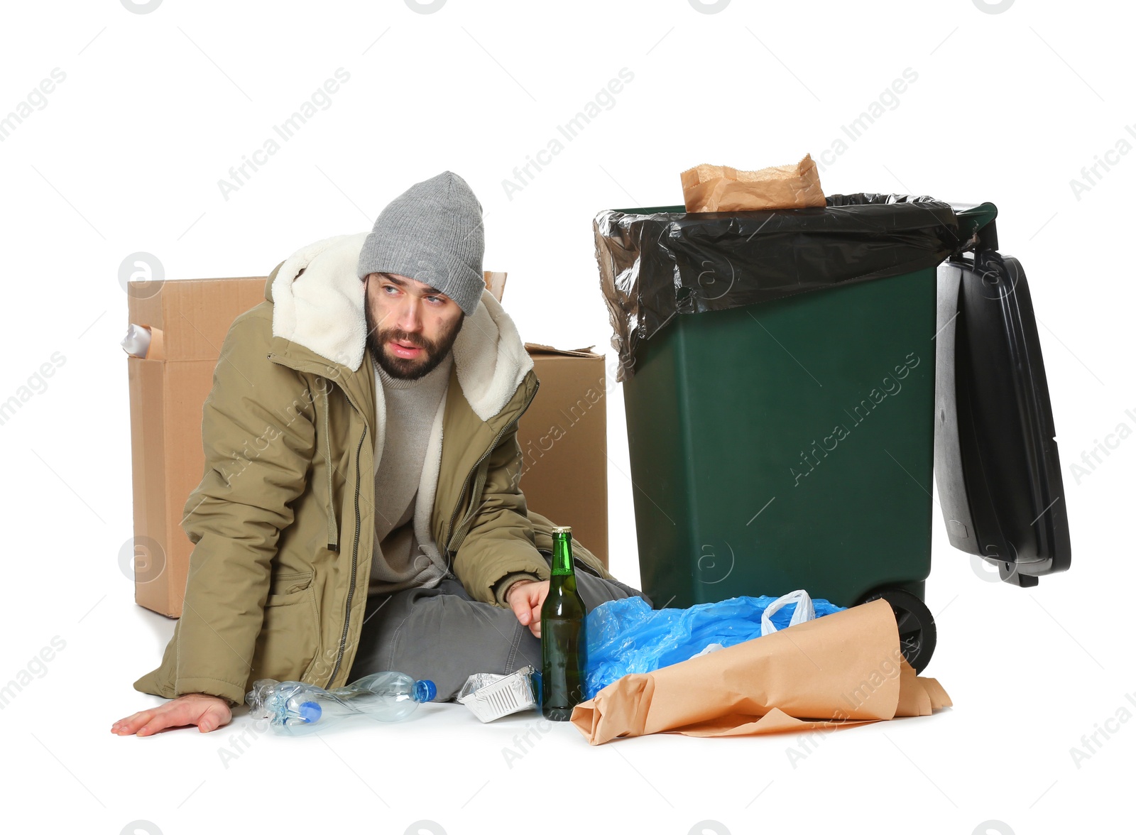 Photo of Poor homeless man sitting near trash bin isolated on white