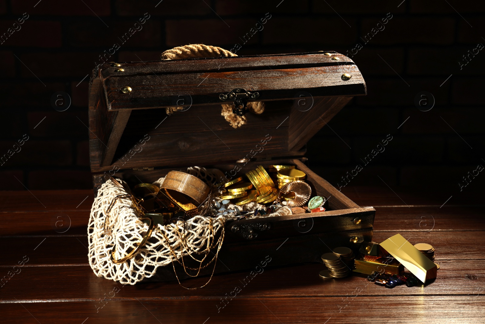 Photo of Treasure chest with net, gold bars, coins, jewelry and gemstones on wooden table