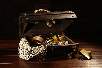 Photo of Treasure chest with net, gold bars, coins, jewelry and gemstones on wooden table