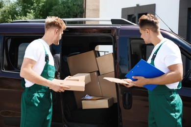 Photo of Young couriers with parcels near delivery car outdoors