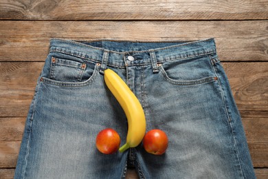 Photo of Men jeans with banana and nectarines symbolizing male genitals on wooden table, top view. Potency concept