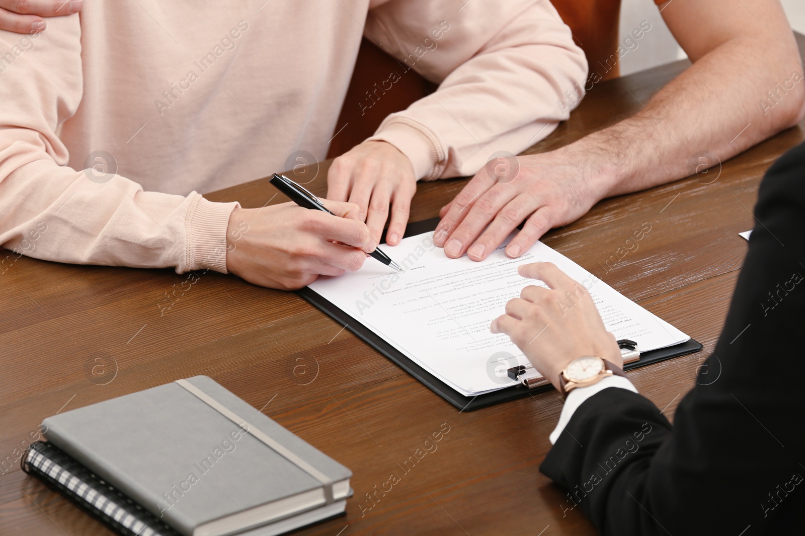 Photo of Notary helping couple with paperwork at wooden table, closeup