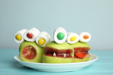 Photo of Delicious apples decorated as monsters on light blue wooden table. Halloween treat
