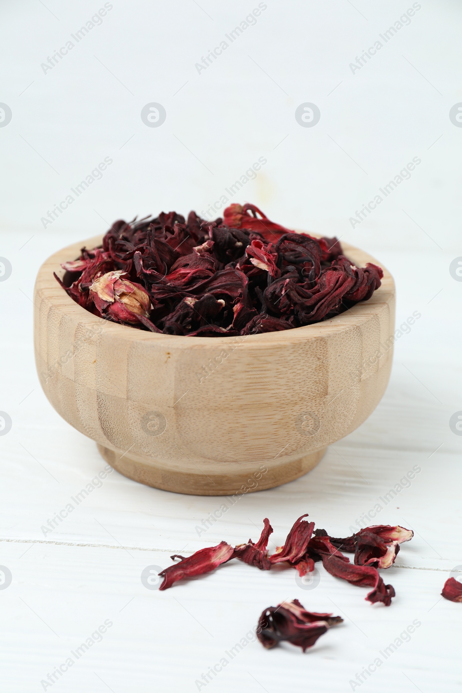 Photo of Hibiscus tea. Bowl with dried roselle calyces on white wooden table