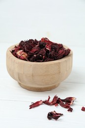Photo of Hibiscus tea. Bowl with dried roselle calyces on white wooden table