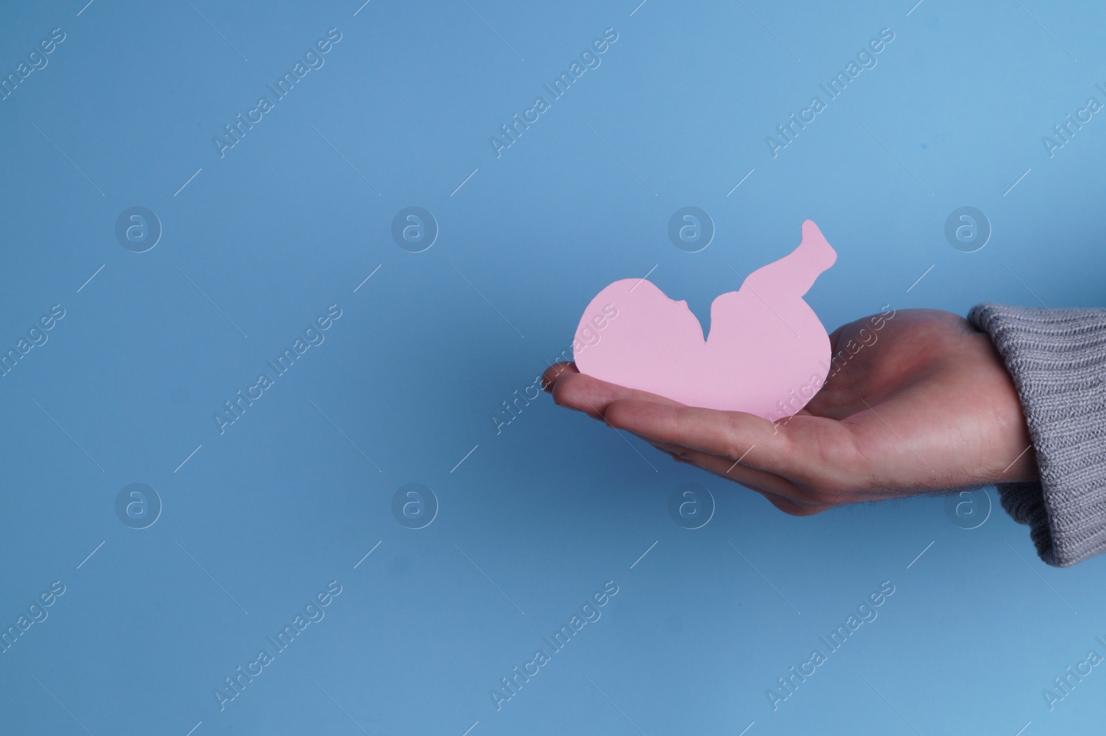 Photo of Female health. Man holding newborn paper figure on light blue background, closeup. Space for text