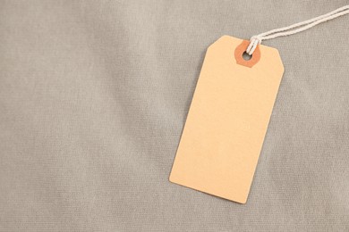 Photo of Cardboard tag on beige garment, top view. Space for text