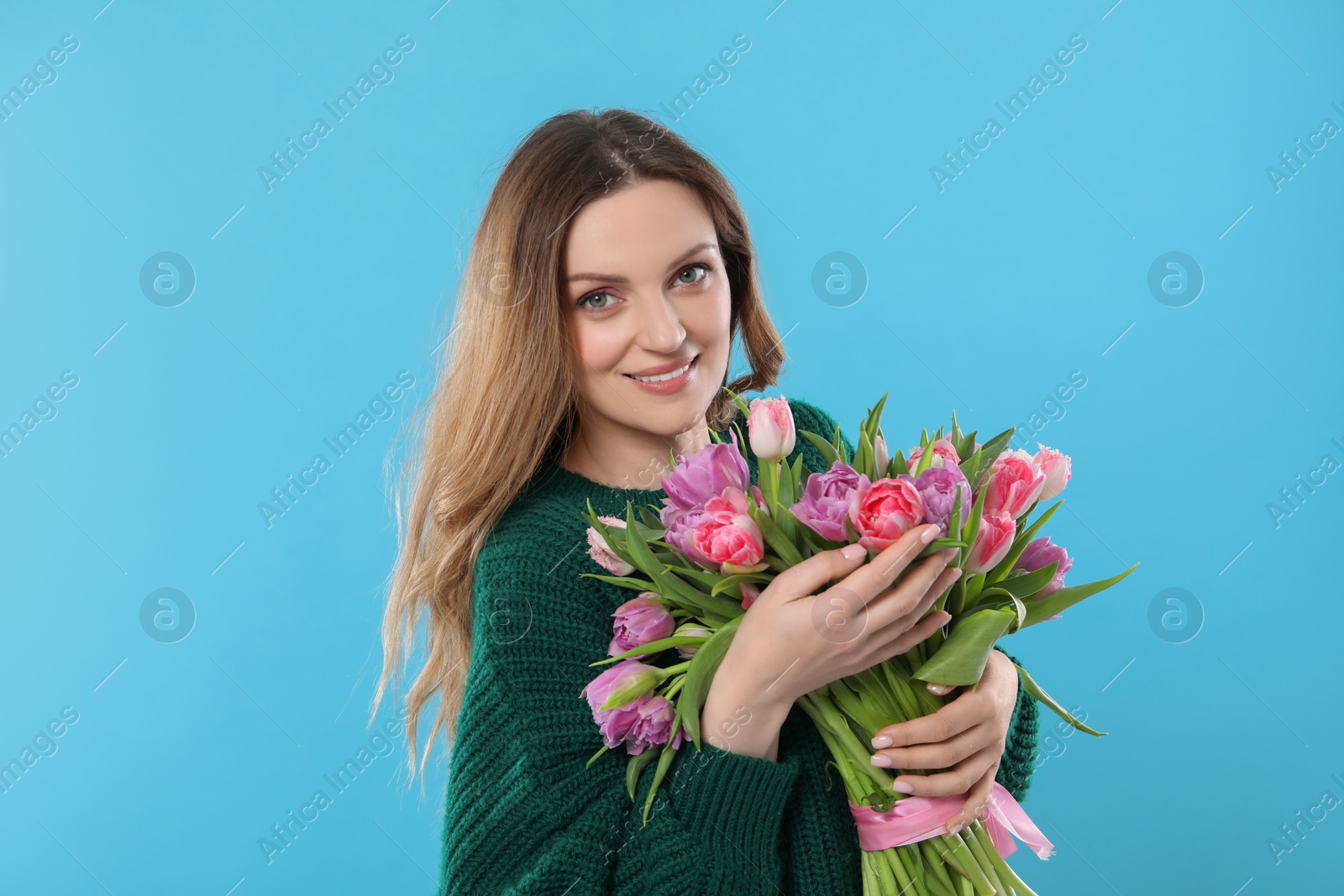 Photo of Happy young woman with bouquet of beautiful tulips on light blue background