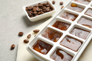 Photo of Ice cubes in tray and coffee beans on grey table, closeup