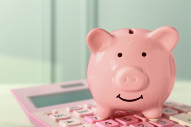 Photo of Ceramic piggy bank and calculator on white table, closeup. Space for text