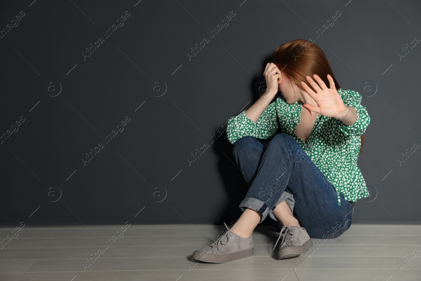 Photo of Young woman making stop gesture while sitting on floor near grey wall. Space for text