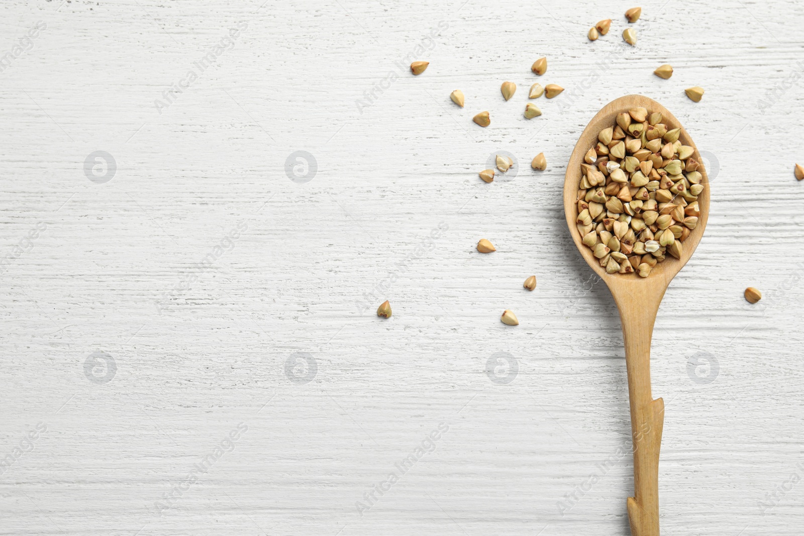 Photo of Uncooked green buckwheat grains in spoon on white wooden table, top view. Space for text