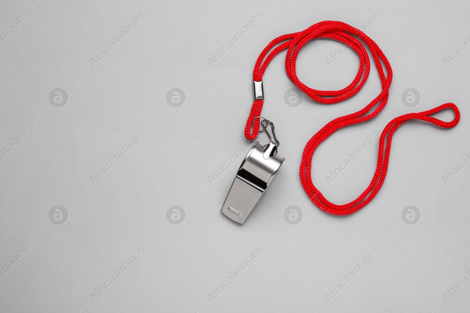 Photo of One metal whistle with red cord on light grey background, top view. Space for text