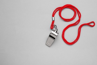 One metal whistle with red cord on light grey background, top view. Space for text