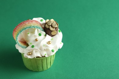 Photo of St. Patrick's day party. Tasty cupcake with sour rainbow belt and pot of gold toppers on green background, closeup. Space for text
