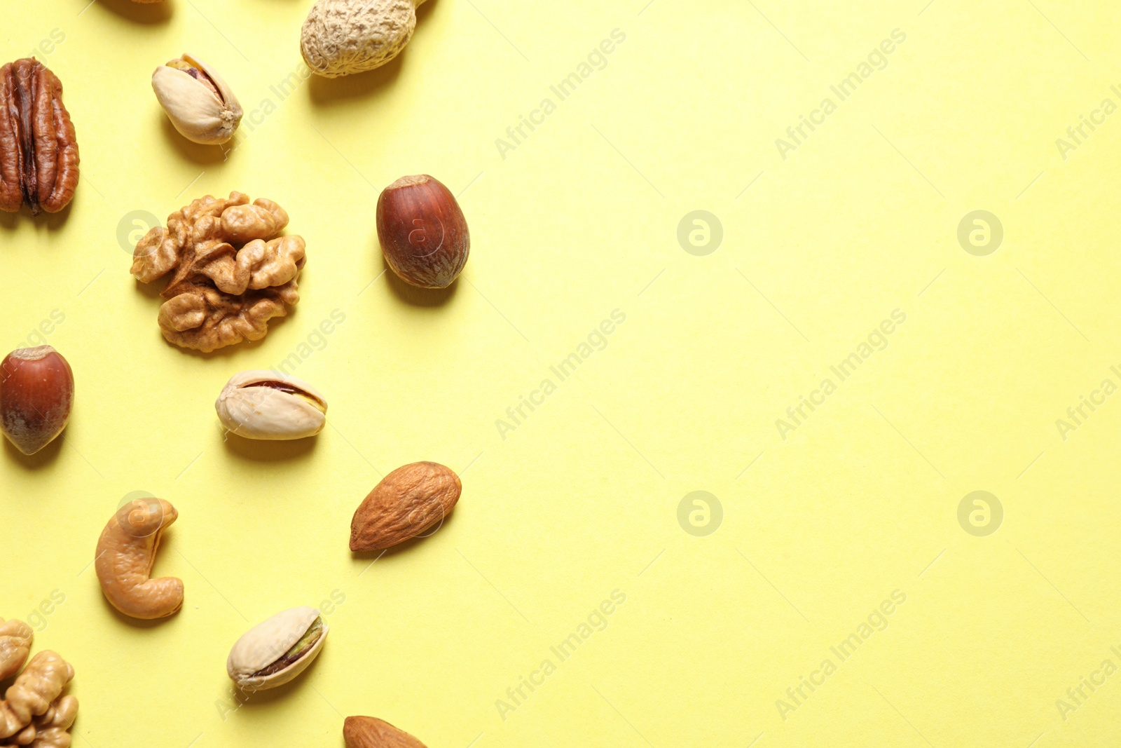 Photo of Different delicious nuts on yellow background, flat lay. Space for text