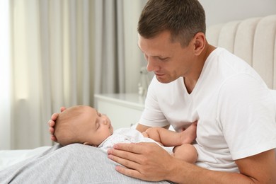 Photo of Happy father holding his cute sleeping baby on bed at home