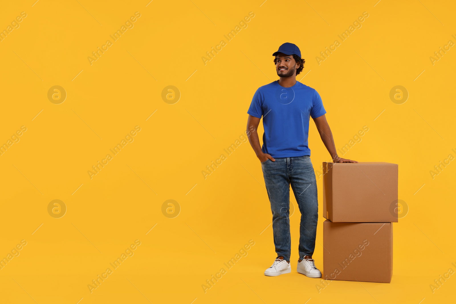 Photo of Happy courier with parcels on orange background, space for text