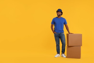 Happy courier with parcels on orange background, space for text