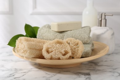 Loofah sponges, soap, towels and green leaves on white marble table