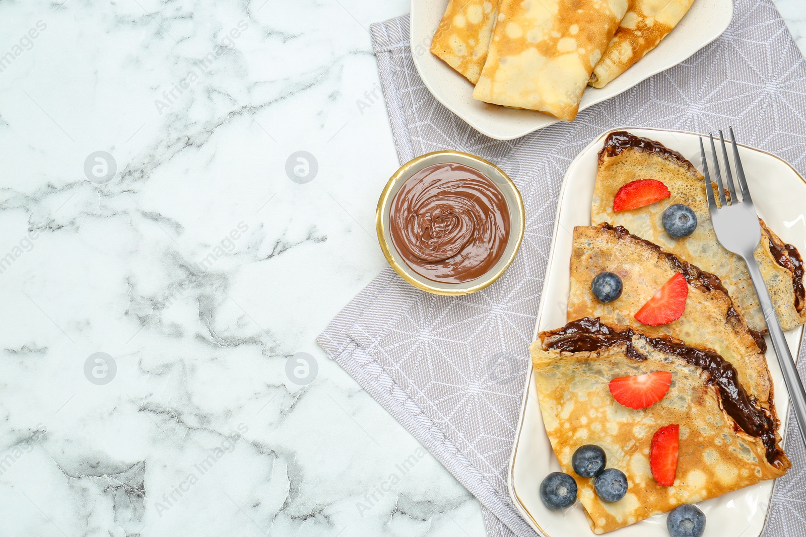 Photo of Tasty crepes with chocolate paste and berries served on white marble table, flat lay. Space for text