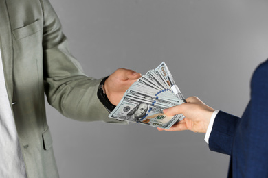 Photo of Woman giving bribe money to man on grey background, closeup of hands